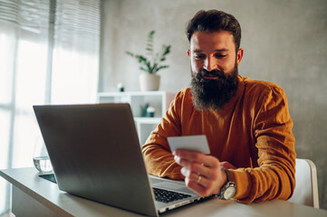 A happy hipster is paying online on an e-banking web app his taxes and home bills while sitting at...