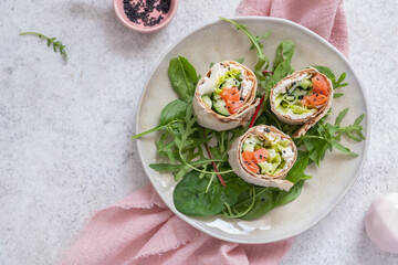 Tortilla with salmon, creamy cheese and vegetables on white plate