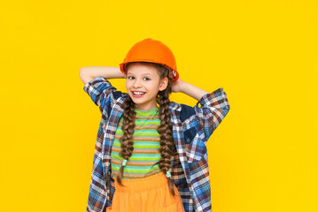 A happy little girl in a construction helmet and shirt on a yellow isolated background. The child is preparing for repairs in the nursery. The profession of an engineer. Yellow isolated background.