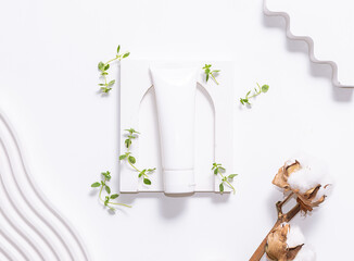 White cosmetic tube with balm, cream or toothpaste on white background with clay decorations, thyme leaves and cotton flowers top view. Eco friendly organic cosmetic concept.