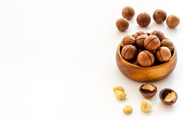 Wooden bowl of raw macadamia nuts in shell. Healthy protein snack background