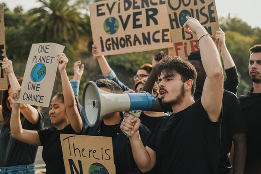 Group of diverse protesters with placards with globe illustrations and megaphone shouting with raised arms during demonstration