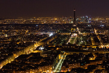 Fototapeta premium Aerial view of Paris at night with a dark Eiffel Tower and La DÃ©fense business district in the background, as seen from the Tour Montparnasse, France