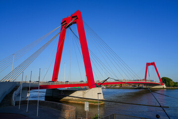 View of the Willemsbrug suspension bridge in Rotterdam, crossing the Nieuwe Maas river in the Netherlands - Red steel road bridge with two towers