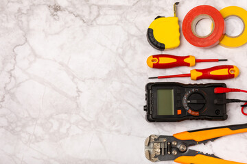 Electrician tools on white marble background.Multimeter,construction tape,electrical tape, screwdrivers,pliers,an automatic insulation stripper,socket and LED lamp.Flatley.electrician concept.Toolbox.