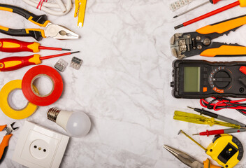 Electrician tools on white marble background.Multimeter,construction tape,electrical tape, screwdrivers,pliers,an automatic insulation stripper,socket and LED lamp.Flatley.electrician concept.Toolbox.