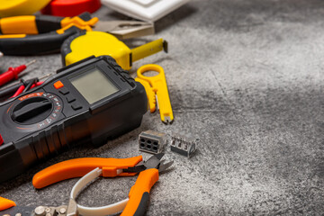 Electrician tools on black marble background.Multimeter,construction tape,electrical tape, screwdrivers,pliers,an automatic insulation stripper, socket and LED lamp.Flatley.electrician concept.