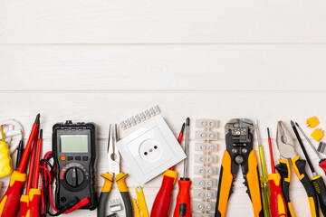 Electrician tools on white wooden background.Multimeter,construction tape,electrical tape, screwdrivers,pliers,an automatic insulation stripper, socket and LED lamp.Flatley.electrician concept.
