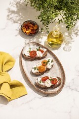 Bruschetta with mozzarella, tomatoes and thyme. Olive oil. Wooden mortar. Light background. Summer snack.