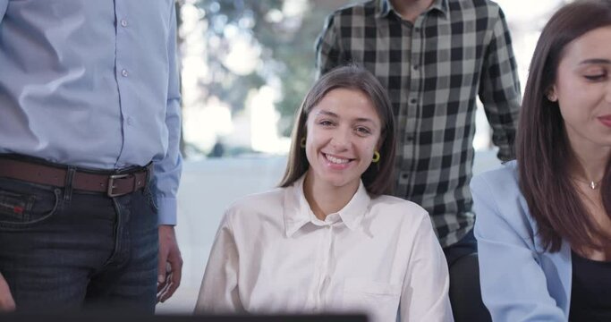 Bussiness team working in an office in front of computer screen. Focus female colleague looking at camera and fooling with funny face expressions.