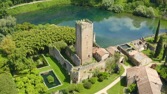 Aerial view of the ruins of the castle and tower located in the Garden of Ninfa, near Latina, Italy. The park is an Italian natural monument and contains a lake and a river. It is empty.