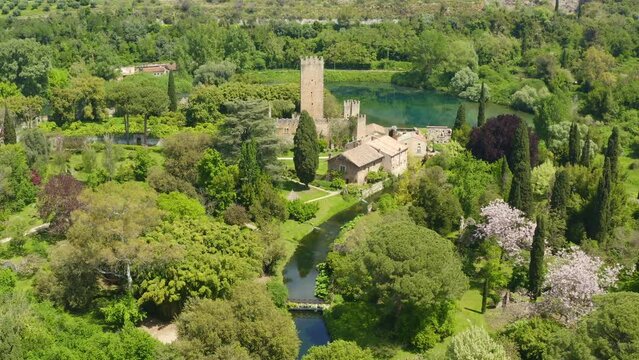 Aerial view of the ruins of the castle and tower located in the Garden of Ninfa, near Latina, Italy. The park is an Italian natural monument and contains a lake and a river. It is empty.
