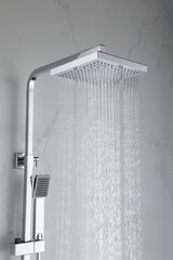 Luxury chromed shower in modern marble bathroom. Square shower head with a perfect water flowing to...