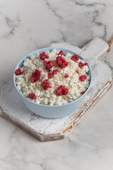 Fresh cottage cheese with raspberries in a bowl on a white background