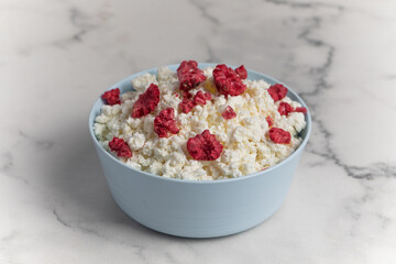 Fresh cottage cheese with raspberries in a bowl on a white background