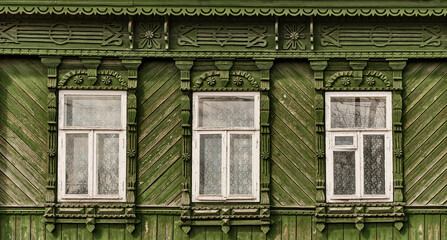 Old wooden windows with carved green architraves on green facade of Russian house.