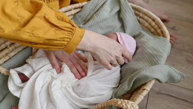 Anonymous mother caressing infant in wicker bassinet