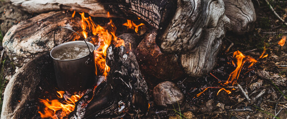 Kettle stands on fire. Cooking food at fire in wild. Beautiful big log burns in bonfire close-up....