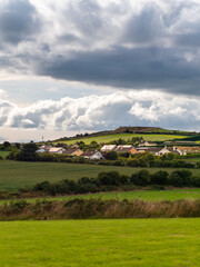 Fototapeta na wymiar Sky with cumulus clouds over a small Irish village on a summer evening. Irish settlement in County Cork, dramatic landscape. European countryside, rustic landscape. Green grass field under clouds, sky
