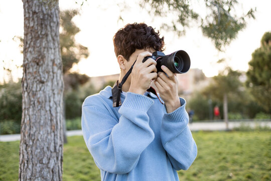 Young man shooting photos near tree on green grass