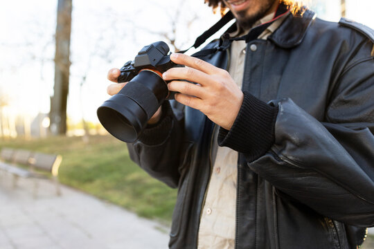 Happy anonymous person taking a photo with a modern camera while standing on a blurred street background