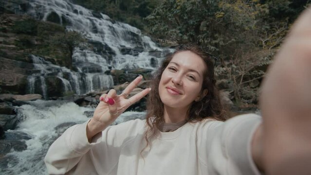 A young woman takes a selfie picture by a majestic waterfall in northern Thailand