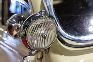 Close-up of the round headlamps of a beige classic car. Beautifully restored chrome details of a...