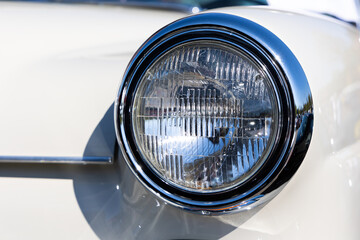 Close-up of the round headlamps of a white classic car. Beautifully restored chrome details of a...