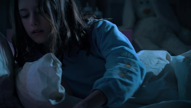Teen girl scrolling social media texting on smartphone in bed in bedroom at night. Technology, internet, communication and people concept. Dependence on social networks in children. Not healthy sleep.