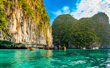 View of long tail boats on turquoise water at ocean near Ko Phi Phi islands, Thailand. Concept of exotic vacation in tropical paradise. Limestone rock in background.