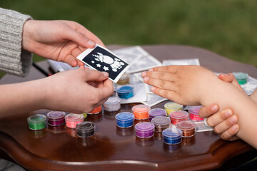 Kid's animator is creating a Shimmering sparkling glitter tattoo on a child's hand at a birthday...