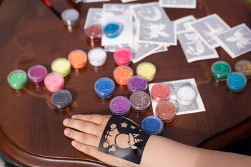 Kid's animator is creating a Shimmering sparkling glitter tattoo on a child's hand at a birthday...