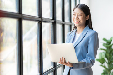 Asian female accountant holding pen working on financial accounting and calculator to calculate business data, accounting documents and laptop computer at office