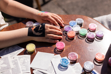 Kid's animator is creating a Shimmering sparkling glitter tattoo on a child's hand at a birthday...