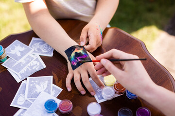 Kid's animator is creating a Shimmering sparkling glitter tattoo on a child's hand at a birthday...