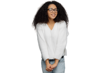 Happy woman with frizzy hair and glasses, wearing white jumper and jeans, keeps hands together, smiles with eyes shut, isolated on grey background. Good emotions concept