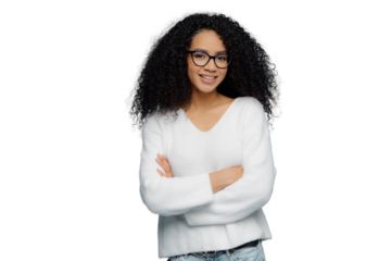 Delighted curly-haired woman in white sweater and jeans stands with folded arms, confident expression. Blue backdrop