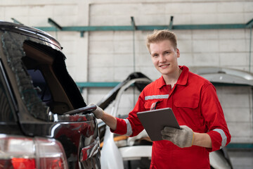 Car mechanic man in red uniform using tablet checking rear window broken of car at garage auto service. Car repair and maintenance concept.