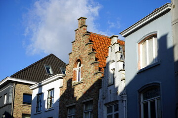 Schmale restaurierte Fassaden alter Häuser mit Treppengiebel vor blauem Himmel im Sonnenschein in der Altstadt von Brügge in Westflandern in Belgien - obrazy, fototapety, plakaty