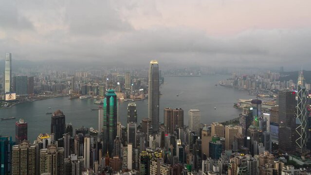 4K Time lapse Panoramic view of Hong Kong City during day to night. View of financial district high-rise and residential buildings lighting up after sunset from Victoria Peak Observation Deck.