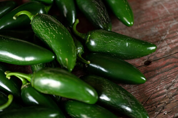 Green hot Jalapeno pepper. Lot of ripe peppers on wooden surface. Pepper harvest. Bright spices. Spicy food. Mexican pepper. Wooden background. Close-up. Soft focus. Top view. High quality photo