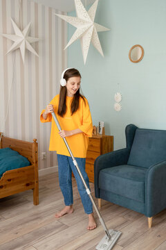 Happy teenager washing floor with mop in bedroom