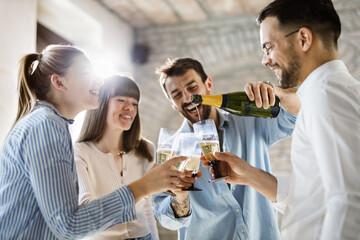 Young business colleagues pouring champagne during a party in the office. Focus is on champagne bottle