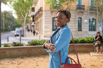 Black business woman smiles and looks at the camera while she is standing in a park of a city