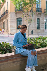 Black business woman is working remotely in a park of a city with a touch laptop