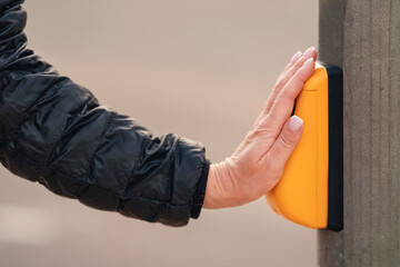 Female hand pressing yellow button at traffic lights on pedestrian crossing at urban street close side view.