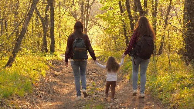 Beautiful young girls lead by hands small child through park. little kid girl daughter holding parents hand walking with them park. happy family life concept. family background sunset forest weekend