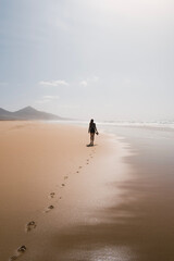 Naklejka premium silhouette of young woman walking at sunset on the wild beach of cofete during her summer trip on the canary island of Fuerteventura