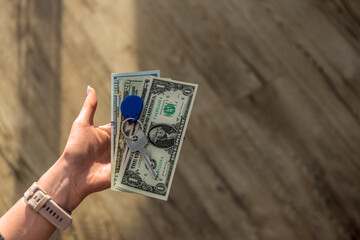 dollars lying on a woman's hand with keys on top, suggesting the idea of buying a property or a home. Concept related to real estate, housing, property management, financial planning, and the