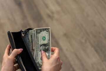 woman counting dollar bills in her wallet, implying the impact of inflation and high prices on her...